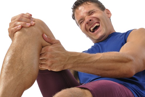 Male athlete on floor clutching knee and hamstring in excrutiating pain on white background